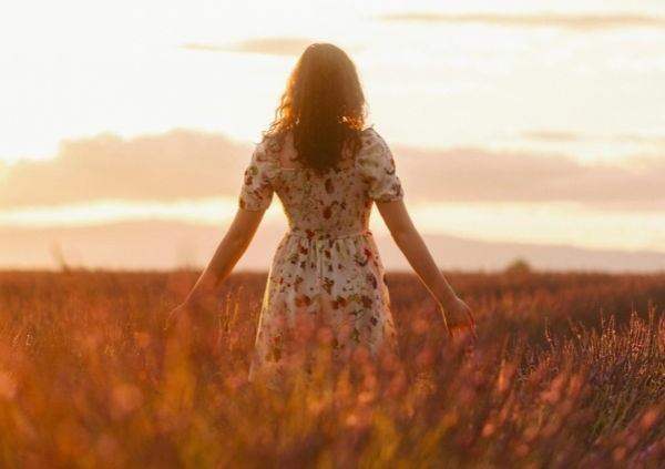 A woman in a white dress with her arms out by her side in a wheat field whilst the sunsets
