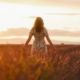 A woman in a white dress with her arms out by her side in a wheat field whilst the sunsets