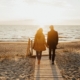 An image of a couple walking on a board walk on a beach.