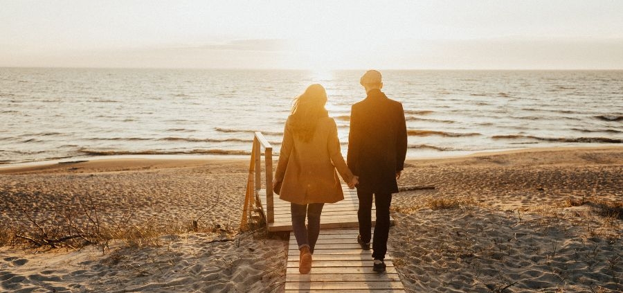 An image of a couple walking on a board walk on a beach.