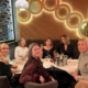 6 Women sat around a table looking at the camera smiling