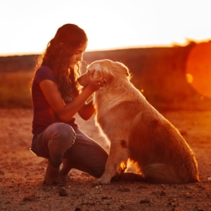 a woman holding her pet dogs head affectionately whilst the sun is setting