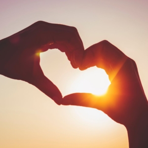 Two hands touching in the sunset, making a heart shape