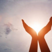 A pair of hands being held in the air whilst the sun shines through