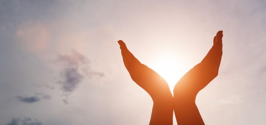 A pair of hands being held in the air whilst the sun shines through