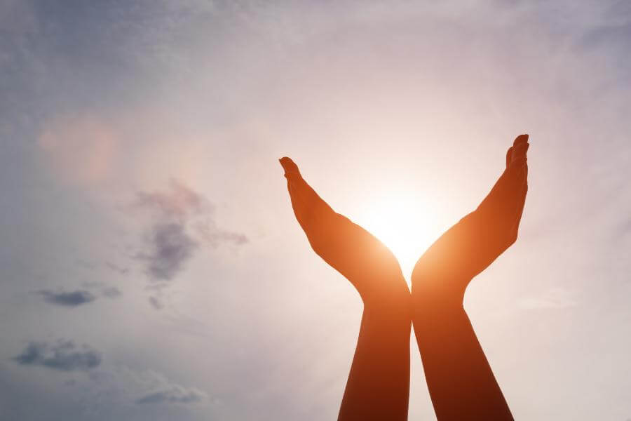 A pair of hands being held in the air whilst the sun shines through