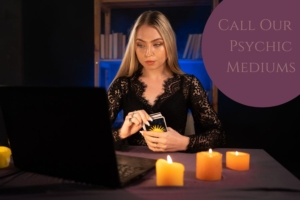 Women holding tarot cards surrounded by candles whilst at a computer