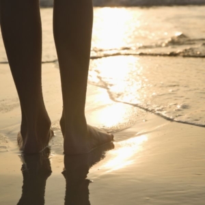 a silhouette of a barefooted woman in wet sand on a beach