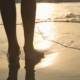 a silhouette of a barefooted woman in wet sand on a beach
