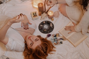 A lady with auburn hair, laying down surrounded by horoscope reading tools