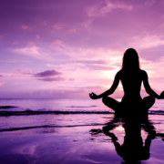 A woman meditating on the beach, by the shore surrounded by purple skies