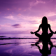 A woman meditating on the beach, by the shore surrounded by purple skies
