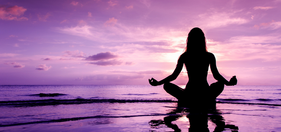 A woman meditating on the beach, by the shore surrounded by purple skies