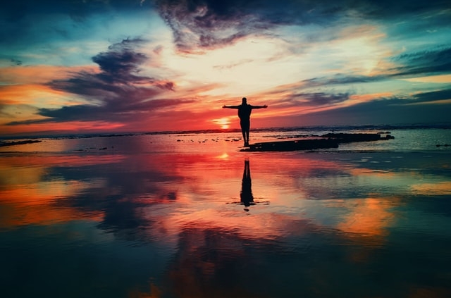 Person standing with arms out during sunset